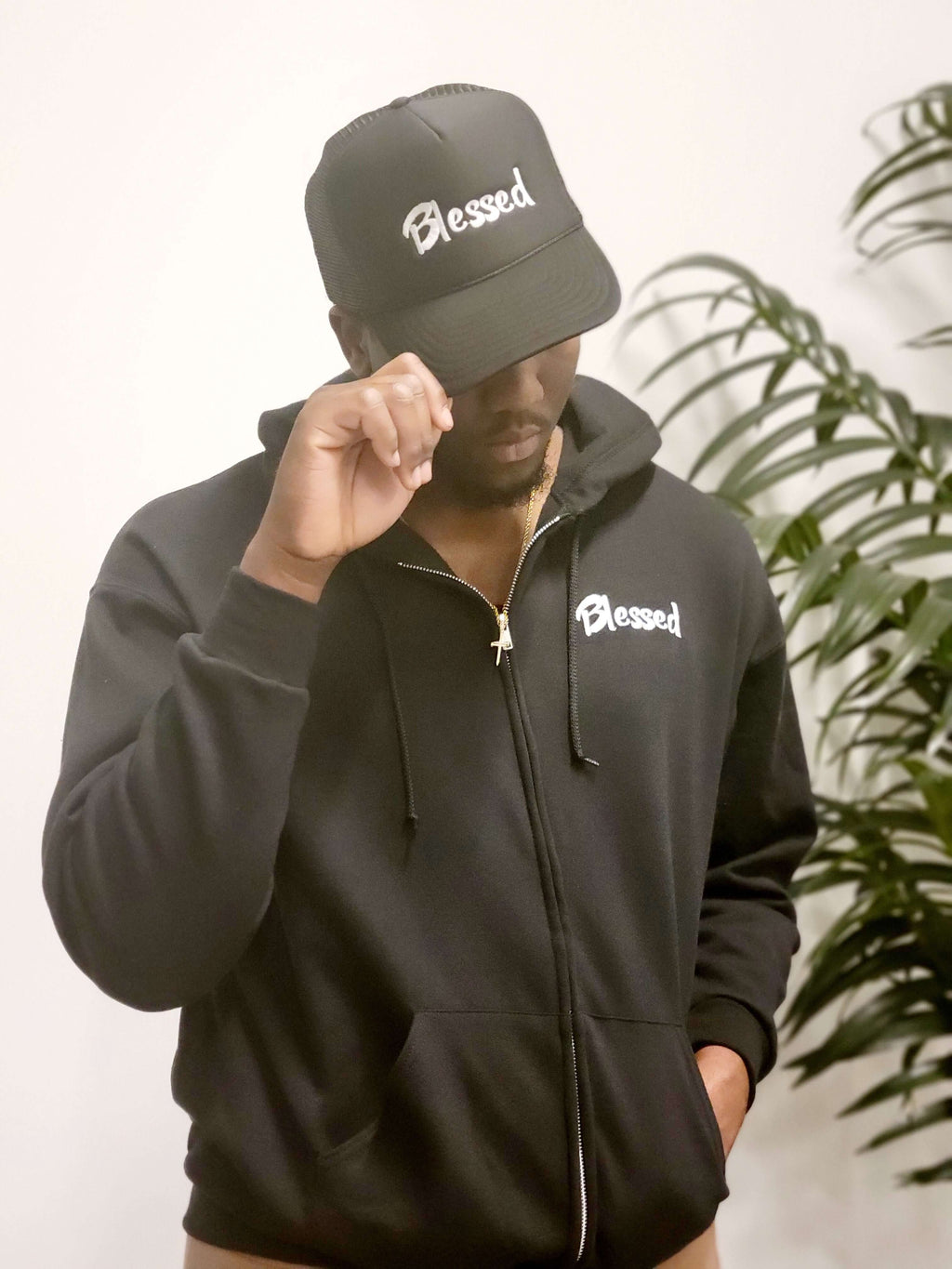 A man in a black hoodie and cap with the word "Blessed" embroidered in white.