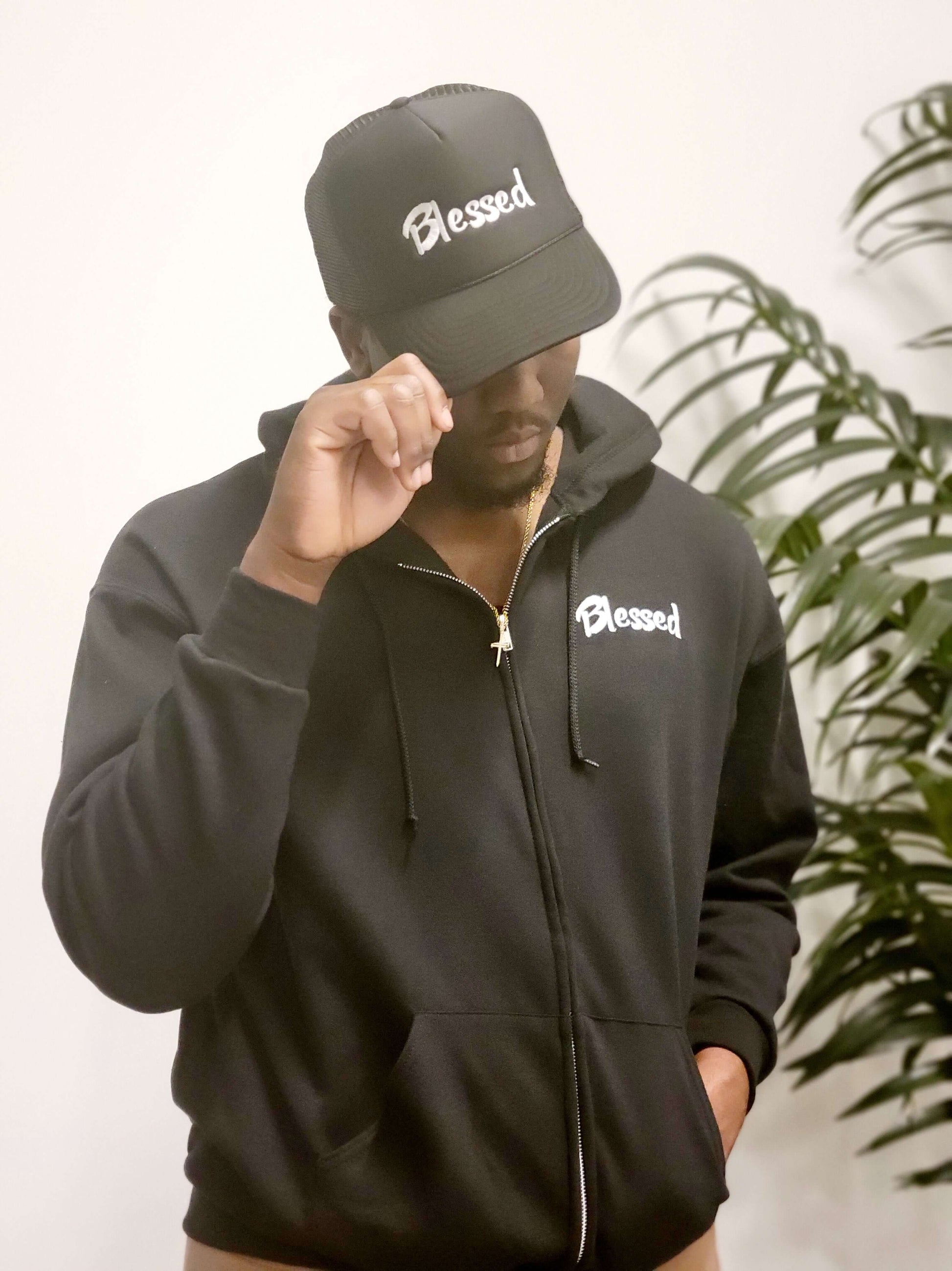 A man in a black hoodie and cap with the word "Blessed" embroidered in white.