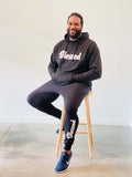A man wearing a Black Unisex Hoodie and black jogger pants with the word "blessed" written in white font.