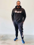 A man wearing a Black Unisex Hoodie and black jogger pants with the word "blessed" written in white font.