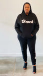 A woman wearing a Black Unisex Hoodie and black jogger pants with the word "blessed" written in white font.